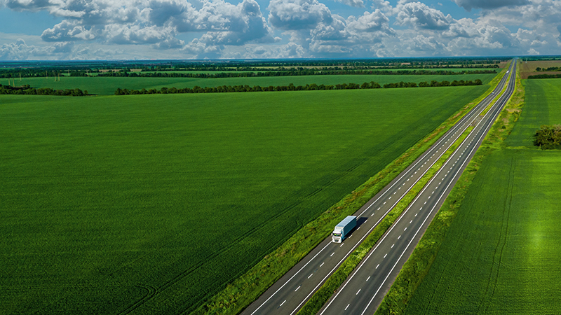 Aerial view truck driving on a road along the green fields