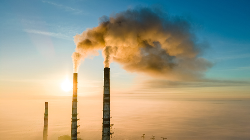 Factory towers with pollution smoke against sunset.