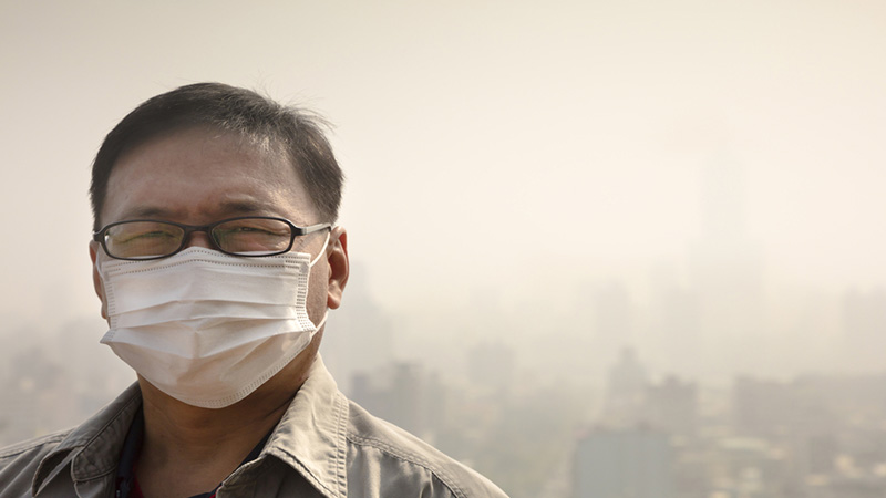 A man wearing a mask due to the smog in a city