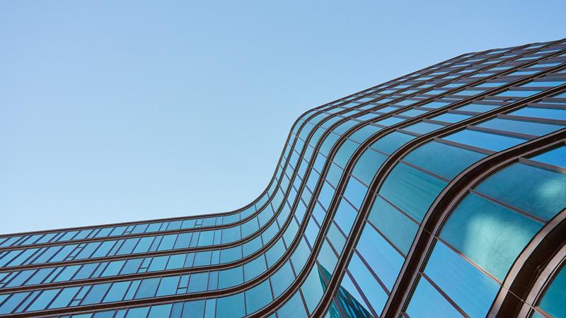 Modern building with curved glass facade reflecting sky.