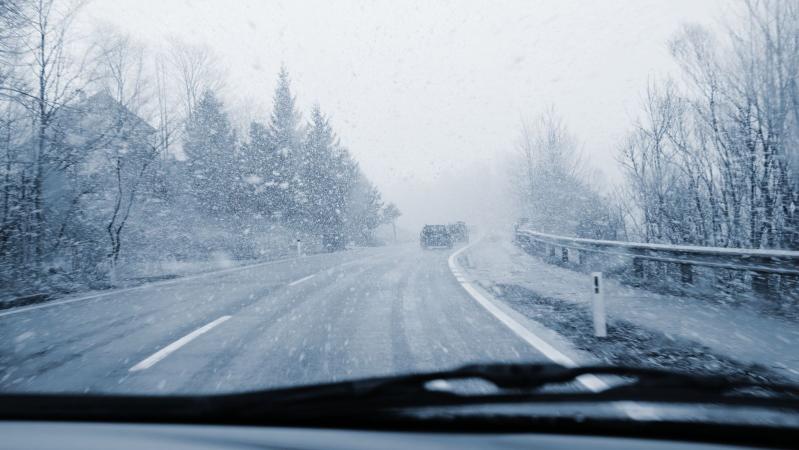 A snowfall and a road viewed from inside a car.