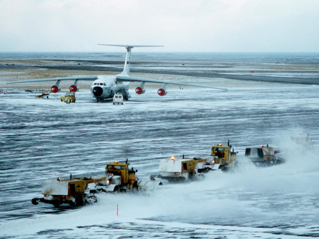Plows clearing a snowy runway with a place on the tarmac in the background