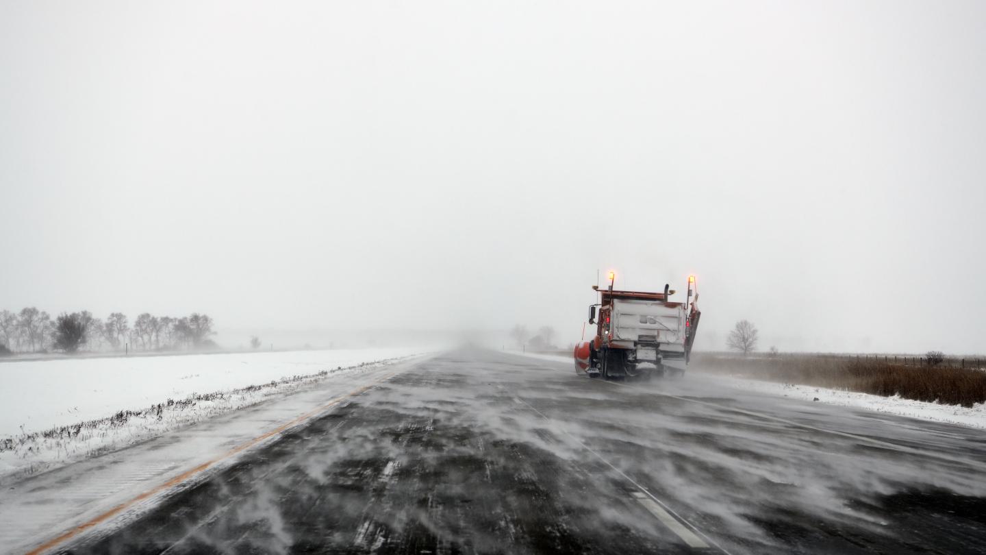 Snow plow driving on road in a snow storm