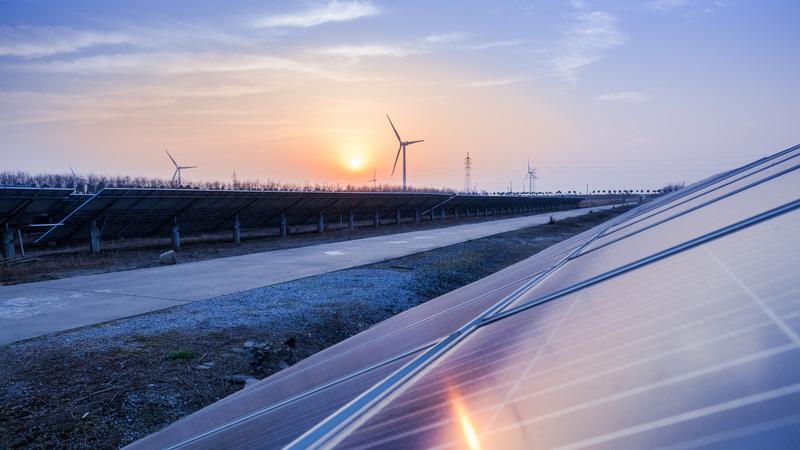 Solar panels and wind turbines in a sunset.