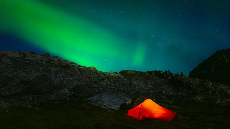Insider camp in darkness of night with green polar lights on sky