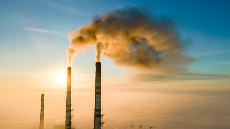 Factory towers with pollution smoke against sunset.