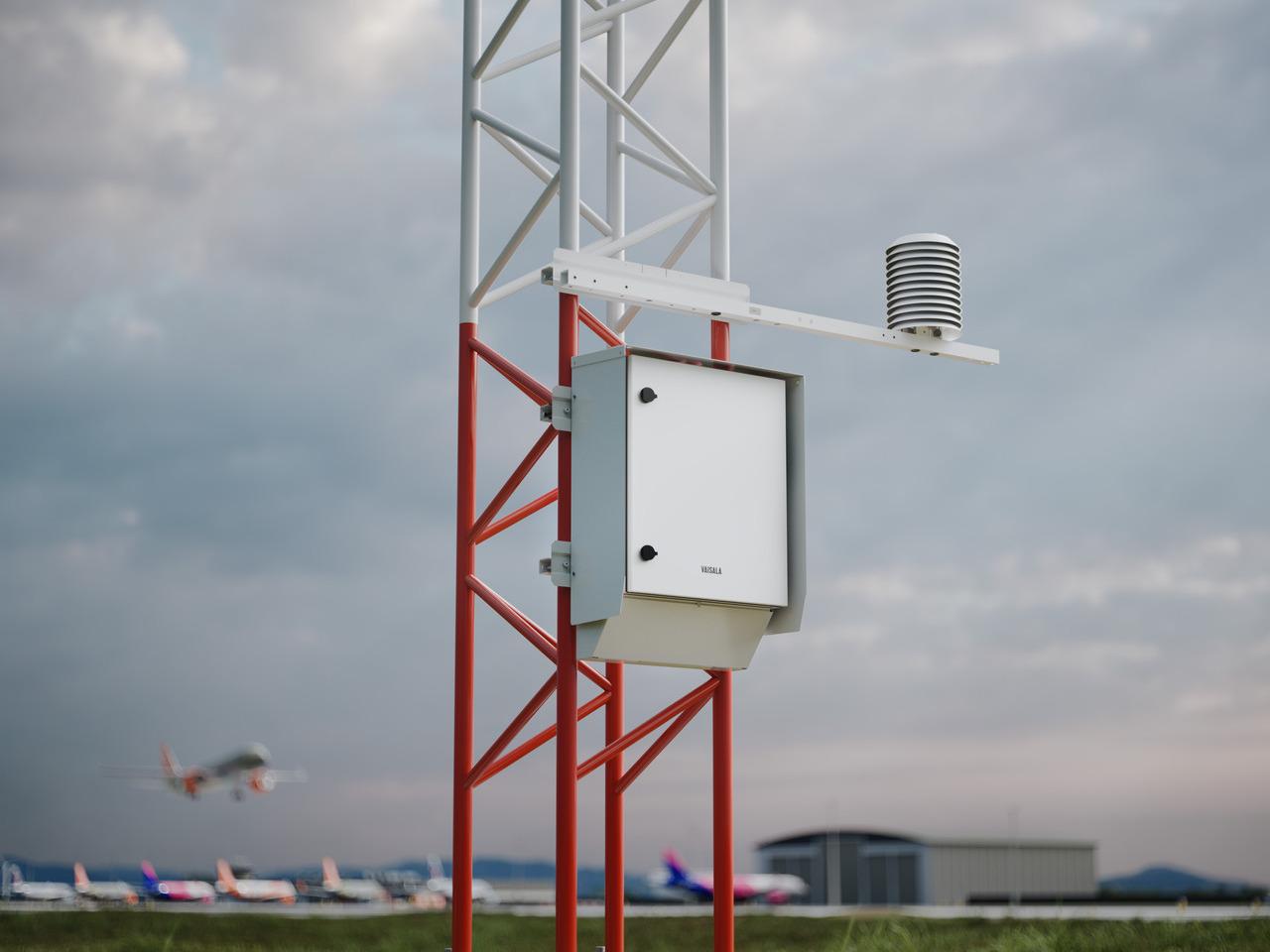 AWS810 pictured at airport with plane flying in the background.
