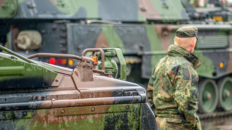 Soldier walking near moving armoured tanks.