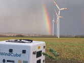 Windcube in field, wind turbines and rainbow in background