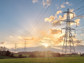Electricity pylons and power lines across a grassy field at sunset