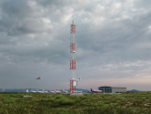 AWS810 pictured at airport with plane flying in the background.