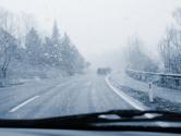 A snowfall and a road viewed from inside a car.