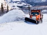 Snow plough truck clearing road after whiteout winter snowstorm blizzard for vehicle access