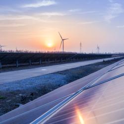 Solar panels and wind turbines in a sunset.