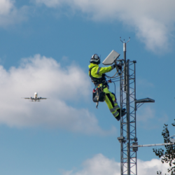 Field technician on RWS200 mast. Airplane in background. 